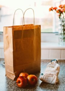A paper bag with apples and packaged goods on a kitchen countertop, lit by natural light.